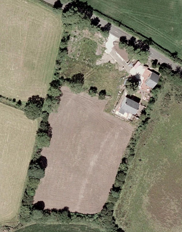 An aerial view showing a rural property with a house and a large rectangular plot of land.