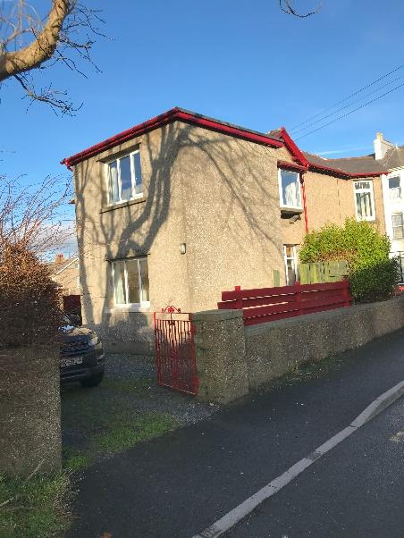 A photograph showing the front elevation of a two-story semi-detached house with pebbledash cladding and red guttering. A car is parked in the driveway behind a low wall and red gate.