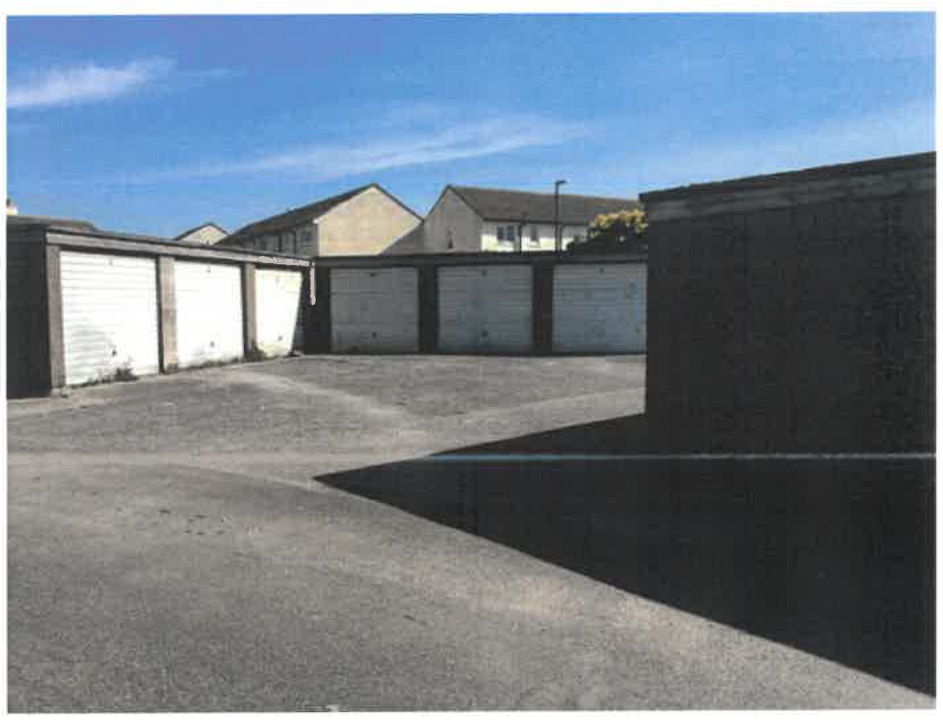 A photograph showing a row of detached garages with white roller doors and a paved parking area in front.