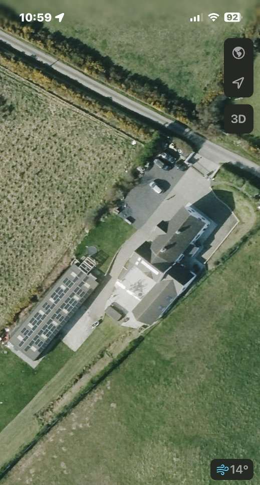 Aerial screenshot from a mobile map application showing a detached house and a separate outbuilding with solar panels in a rural setting.
