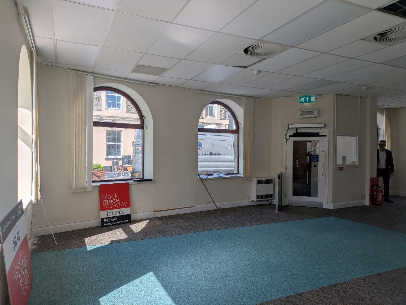 Interior photograph of a commercial property with arched windows and a 'for sale' sign.