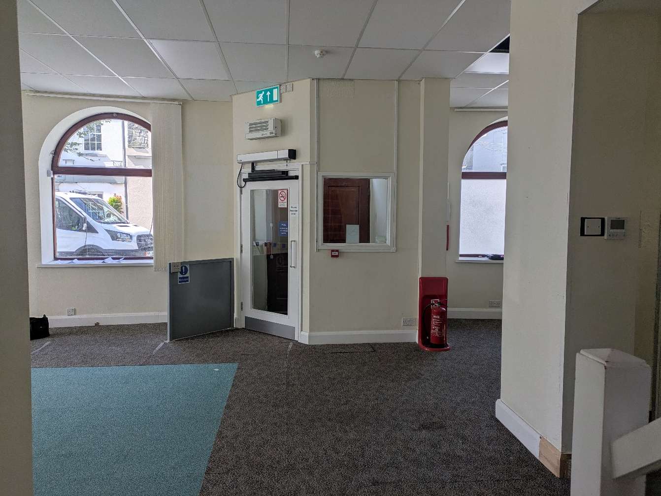 Interior photograph of a commercial or office space featuring arched windows, a glass entrance door, and carpeted flooring.