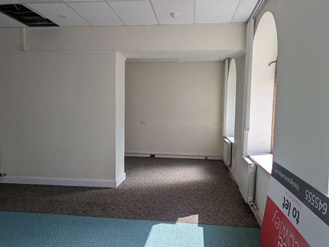 Interior photograph of an empty commercial room featuring arched windows and carpeted flooring.