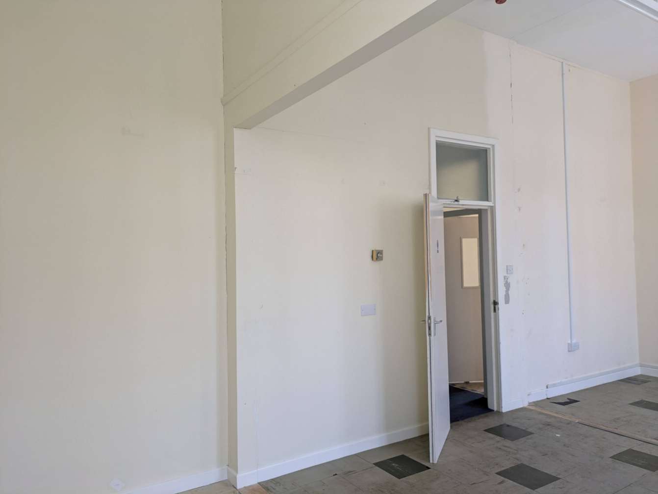 Interior photograph of a room with white walls, a large ceiling beam, and an open doorway featuring a transom window.