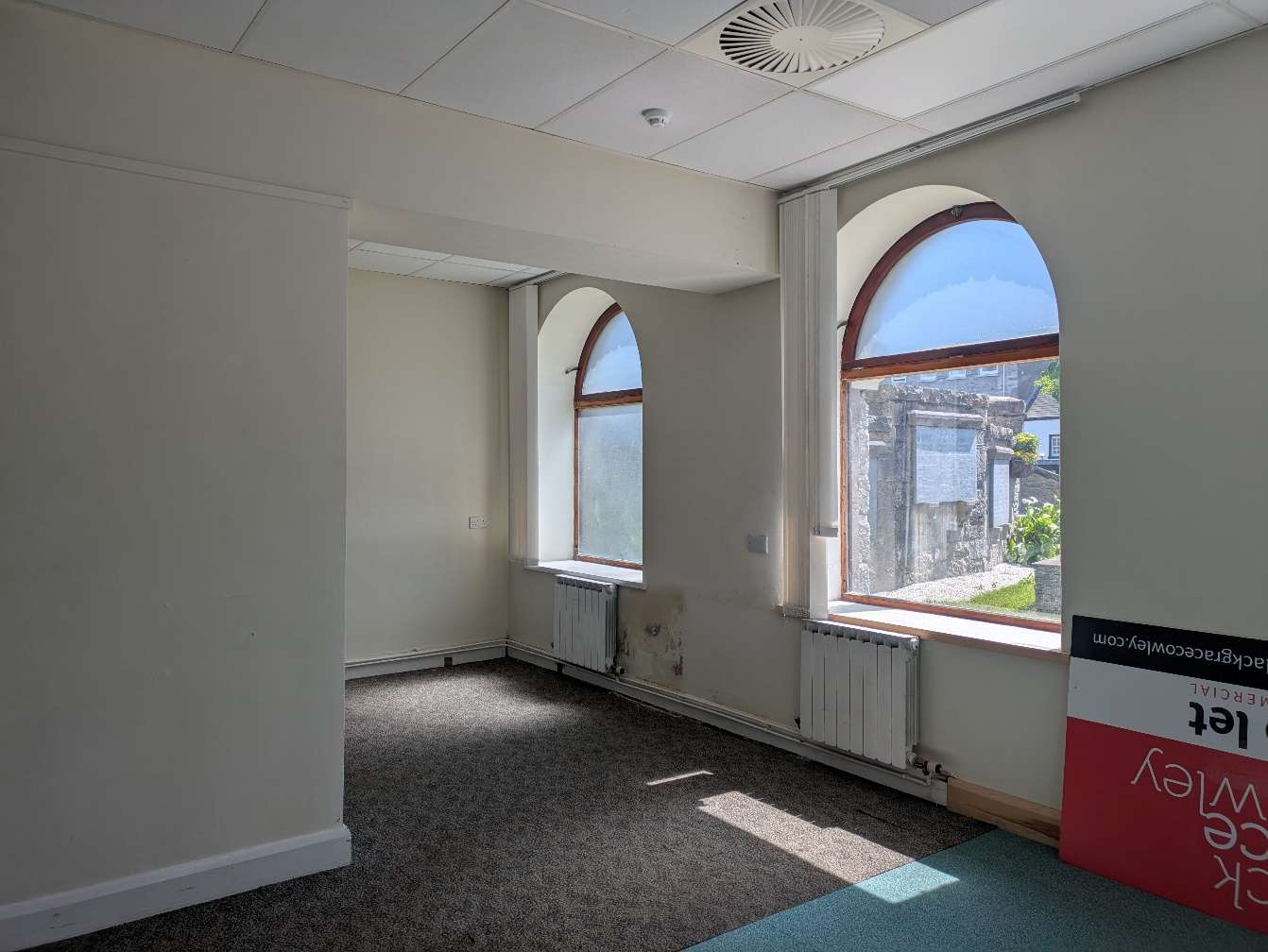 Interior photograph of a commercial room featuring large arched windows, drop ceiling, and carpeted flooring.