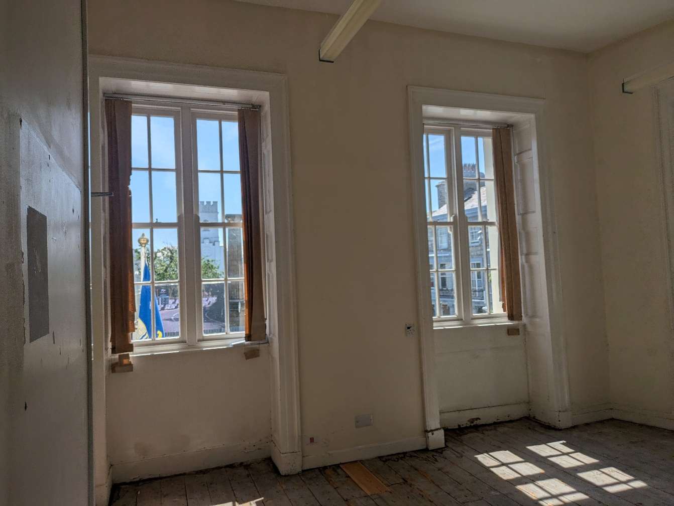 An interior photograph of a room featuring two large traditional sash windows and wooden floorboards, likely captured during a renovation or repair project.