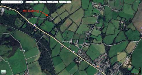 An aerial map view showing a rural landscape with green fields and a road, highlighting a specific building labeled 'Mill Building' with a red arrow.