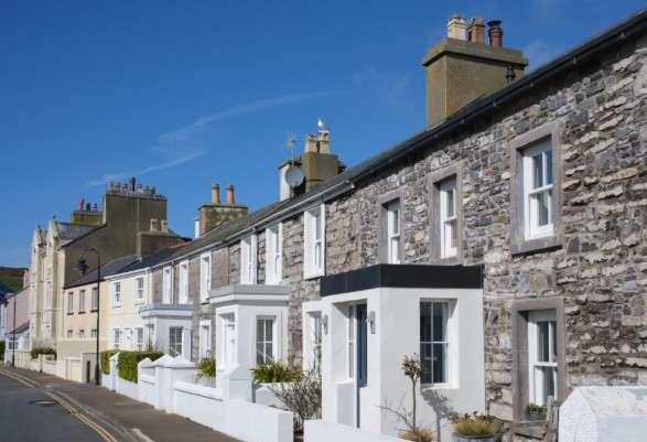 A street-level photograph showing a row of traditional stone terraced houses with chimneys under a clear blue sky.