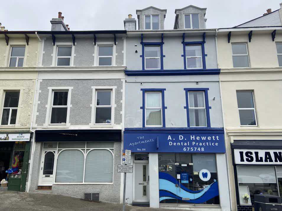 A street-level photograph showing a row of terraced buildings, featuring a dental practice shopfront with blue signage and a residential entrance.