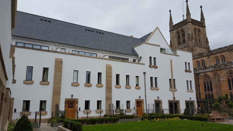 Exterior photograph of a large white building with stone accents situated next to a historic stone church with spires.