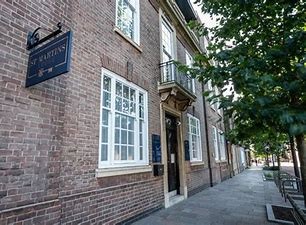 A street-level photograph showing the brick facade of a building with white sash windows, a small balcony, and a hanging sign reading 'The Planters'.