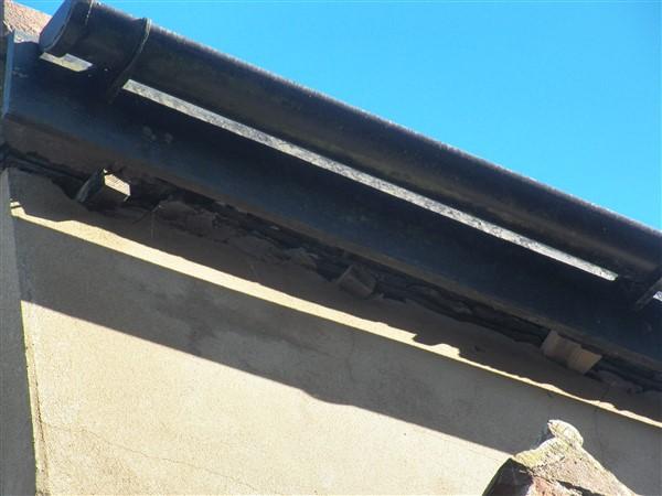A close-up photograph showing a black pipe running along the top of a rendered wall with a visible gap underneath against a blue sky.