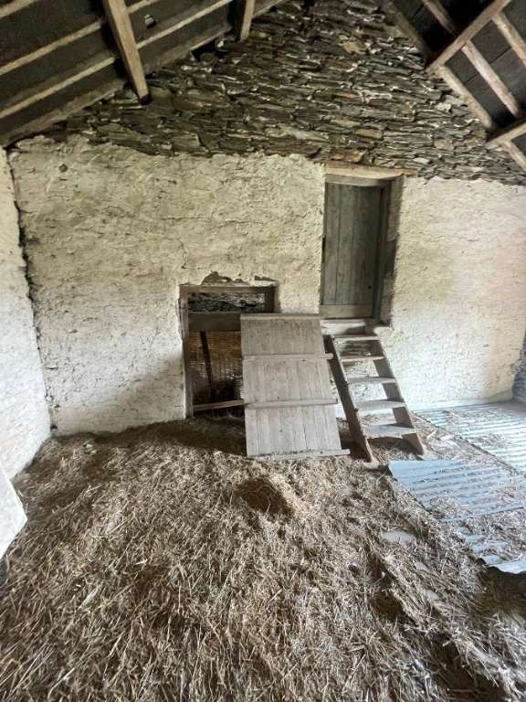 Interior photograph of an agricultural barn featuring a floor covered in hay, rough walls, and a traditional stone slate roof with wooden beams.