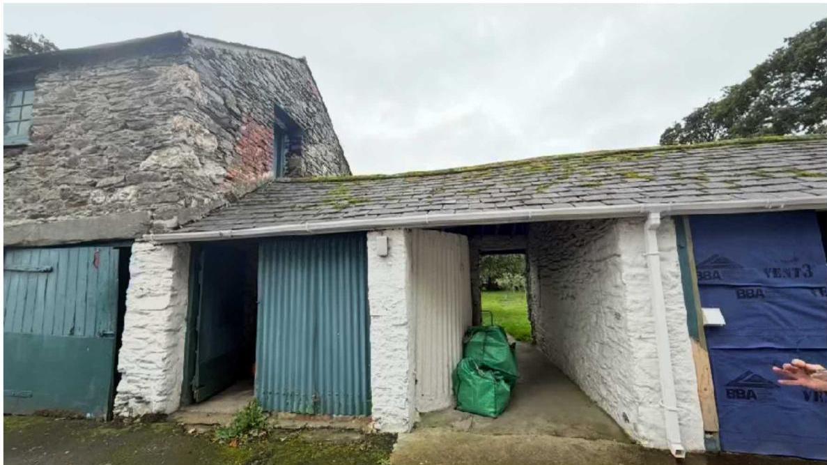 A photograph showing a stone building with a lower, single-storey attached structure featuring white rendered walls and a slate roof, likely a barn conversion site.