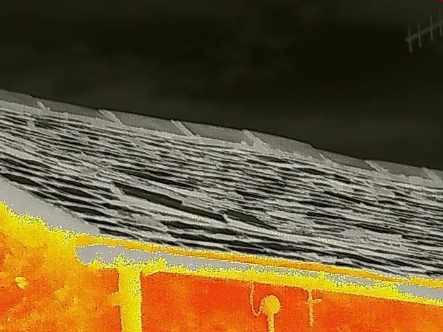 A close-up photograph showing the edge of a slate roof with a gutter and fascia board, possibly with thermal imaging characteristics.
