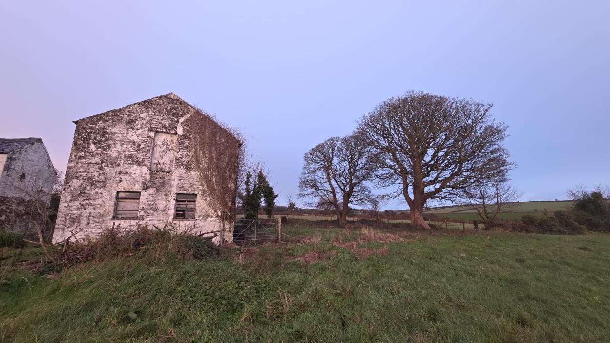 A photograph showing a dilapidated stone building, likely a barn, with boarded windows in a rural grassy field.