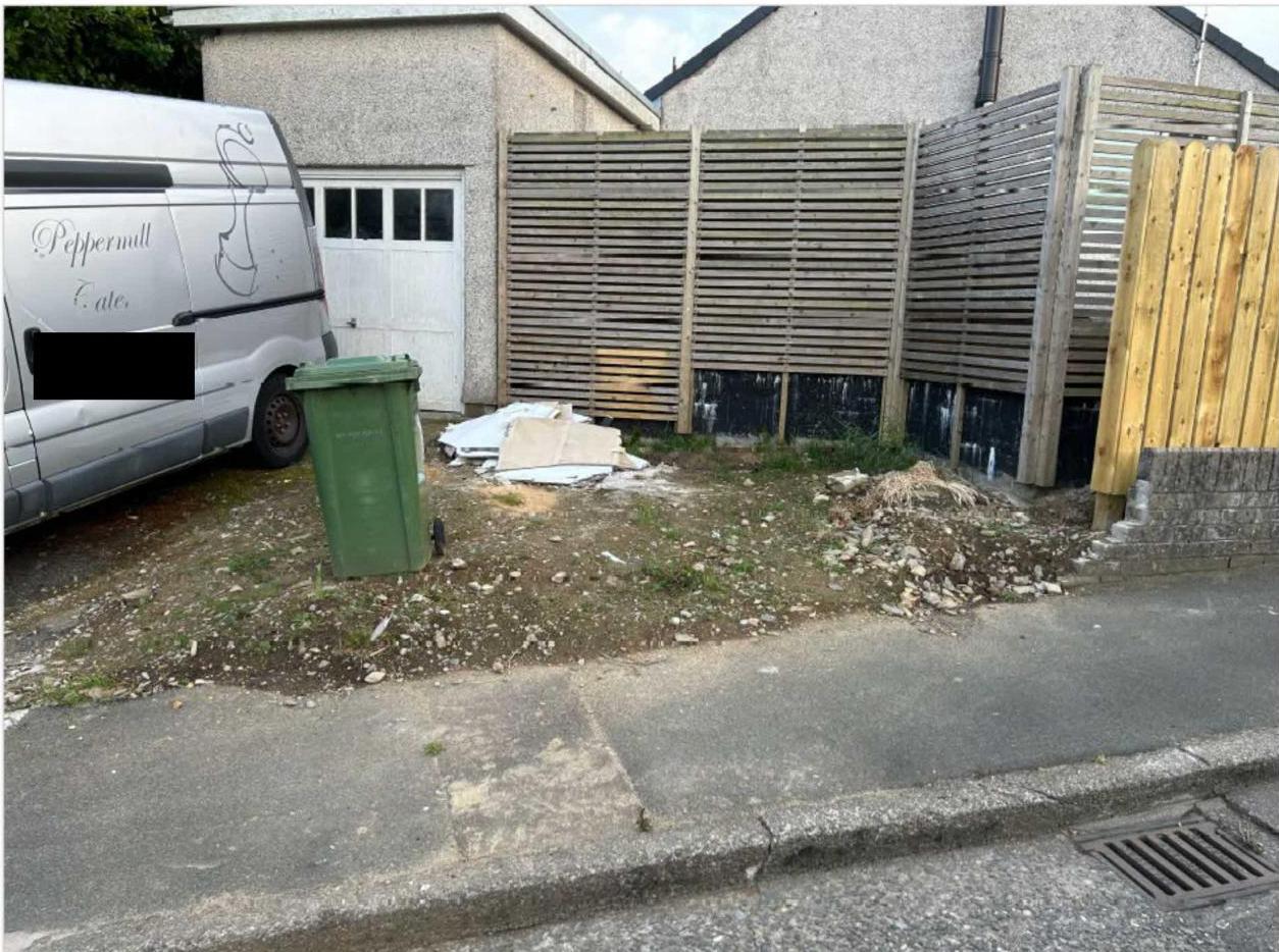 A photograph showing a residential property with a newly installed wooden slatted fence and a white garage door. A white van is parked on the left, and the ground appears to be a driveway or hardstanding area.