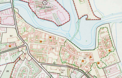 This image displays a planning site location map showing a coastal or riverside area with a network of roads, building footprints, and a significant water body.