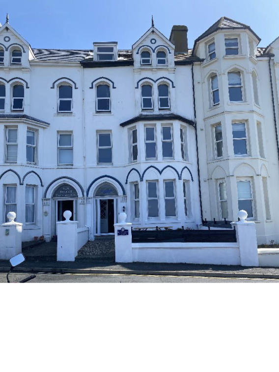 A street-level photograph showing the front elevation of a large white terraced building, identified by a sign as the Royal Hotel, featuring bay windows and arched architectural details.