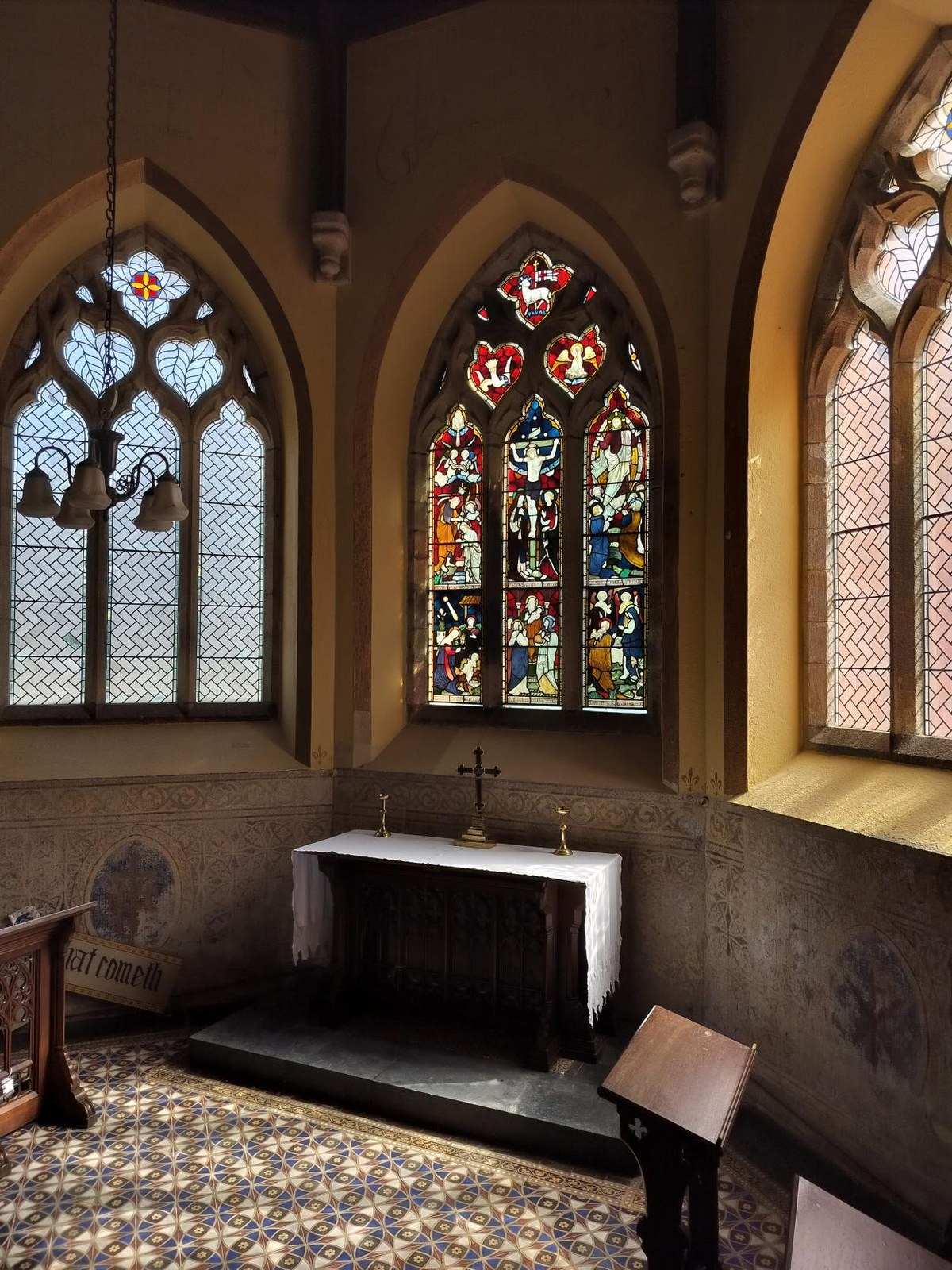 Interior photograph of a chapel showing an altar, cross, and stained glass windows with patterned floor tiles.