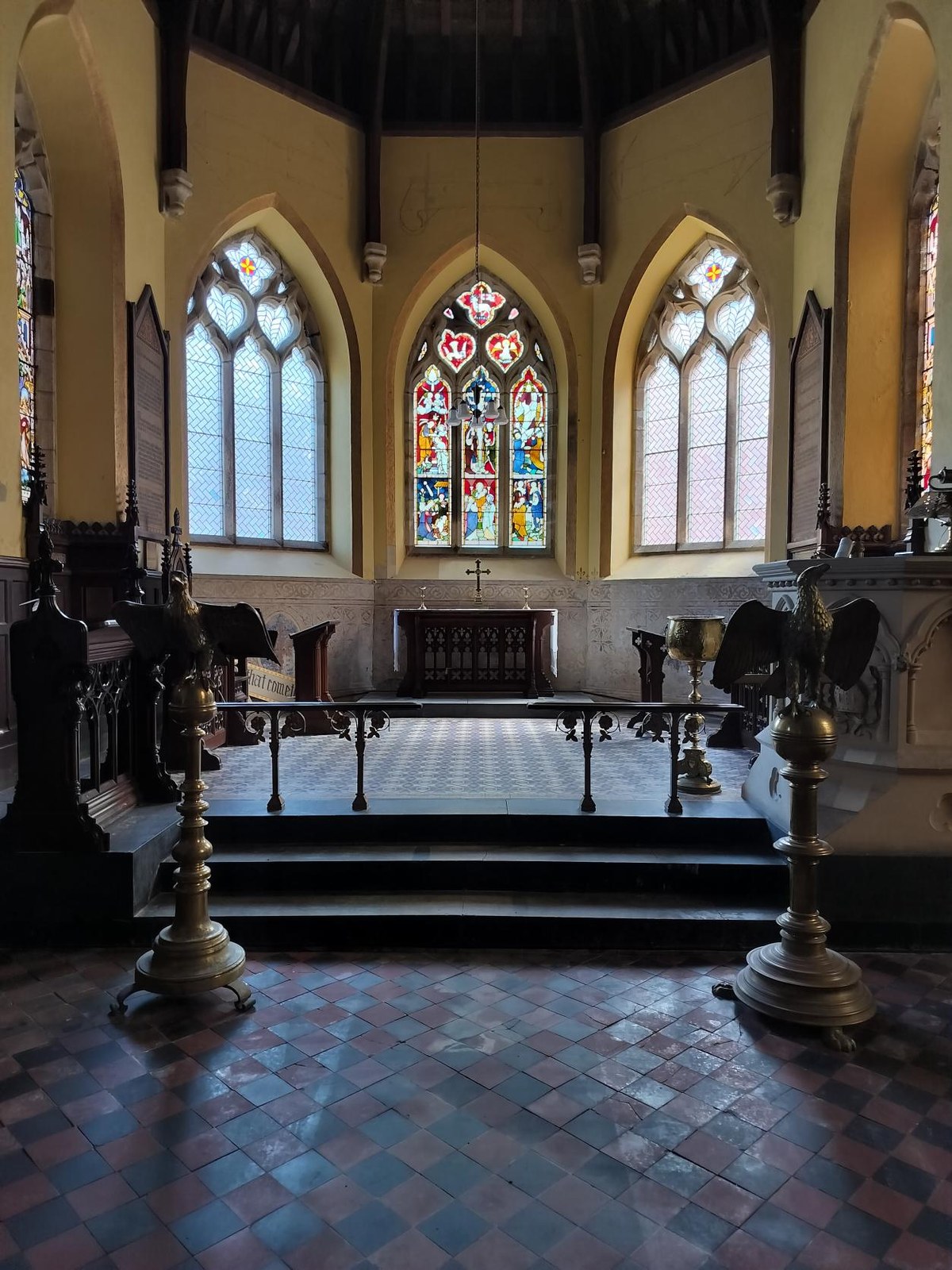 The image shows the interior of a chapel featuring an altar, ornate stained glass windows, and a checkered tile floor.
