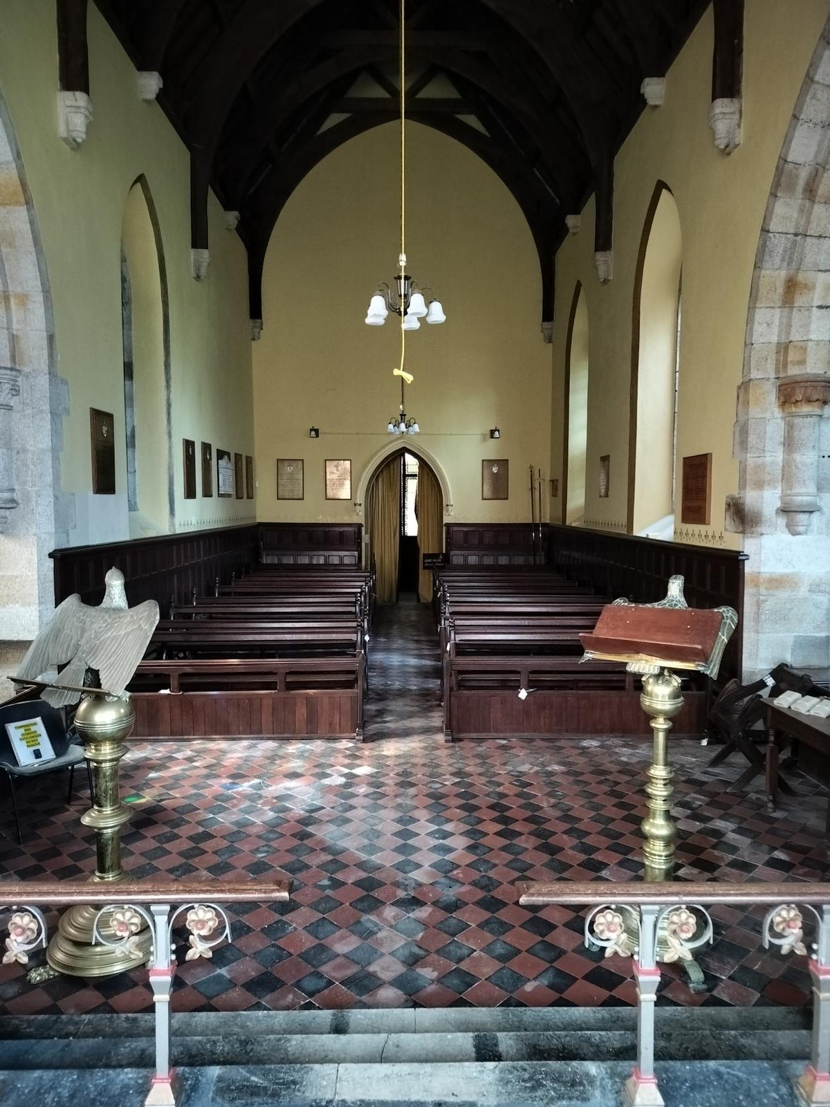 Interior view of a historic chapel featuring rows of wooden pews, a checkered tile floor, stone arches, and a dark timber ceiling.