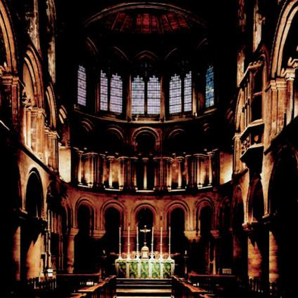 Interior photograph of a historic stone chapel featuring arched windows, stone walls, and an altar area with candles.