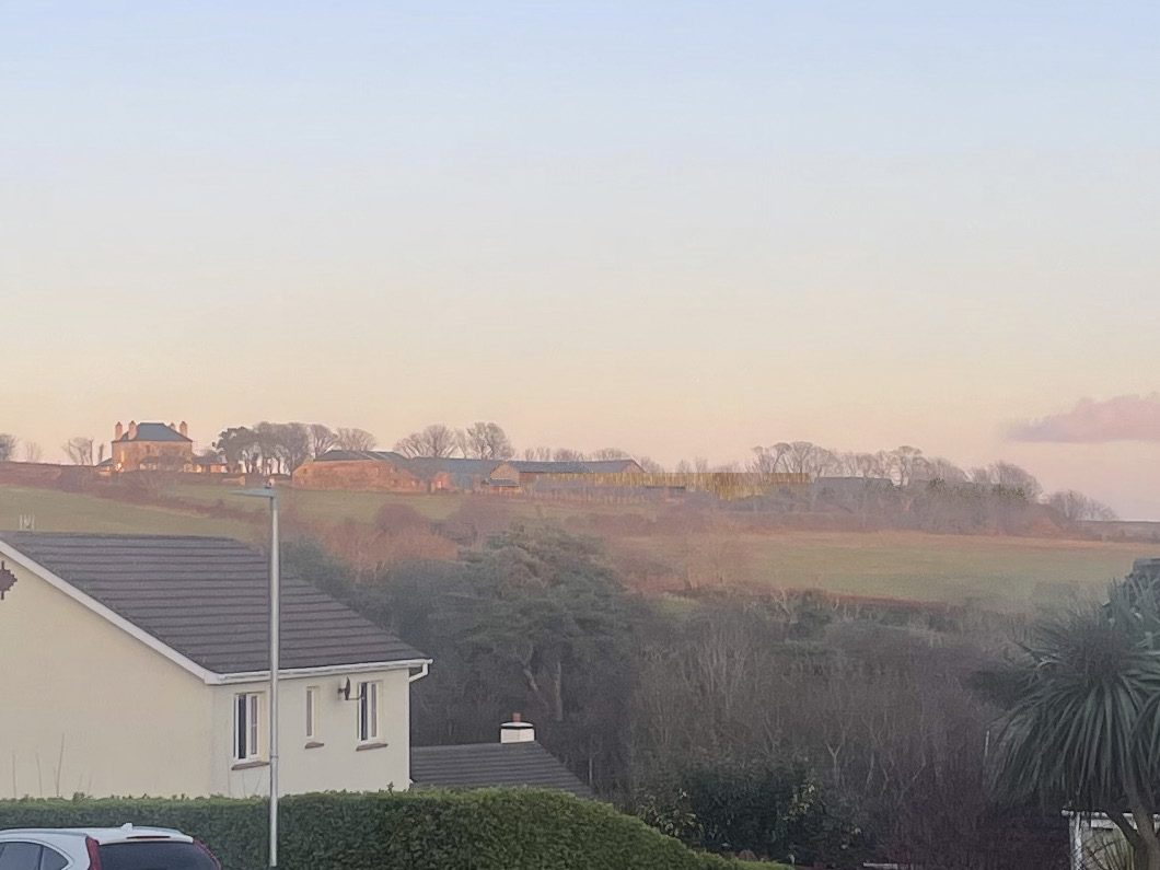 A photograph showing a rural landscape with a residential house in the foreground and agricultural buildings on a hill in the distance.