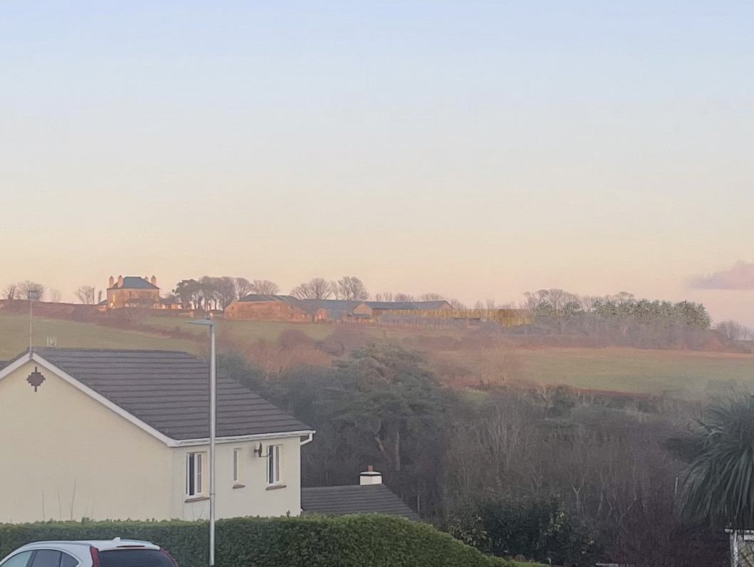 A photograph showing a white residential house in the foreground overlooking a grassy hillside with distant farm buildings in the background.