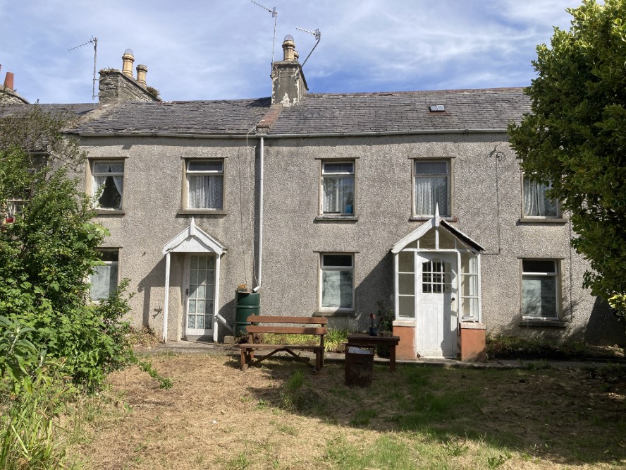A photograph showing the front elevation of a terraced stone house with white porches and a garden area in the foreground.