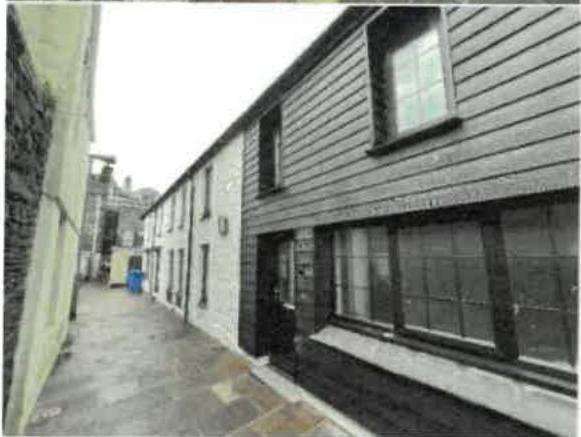 A black and white photograph showing the rear elevation of a two-story building with horizontal cladding, viewed from a narrow paved alleyway.
