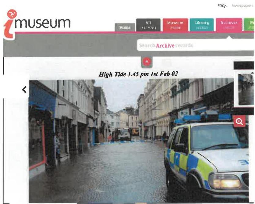 A screenshot of a museum archive webpage displaying a photograph of a flooded street with a police car during high tide.