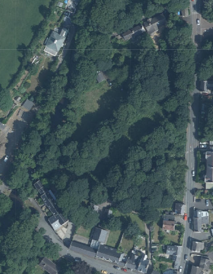 An aerial site location map showing a large, densely wooded plot of land surrounded by residential properties and a road.