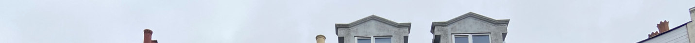 A low-angle panoramic photograph showing the upper storey of a terraced building with grey bay windows and chimneys against a cloudy sky.