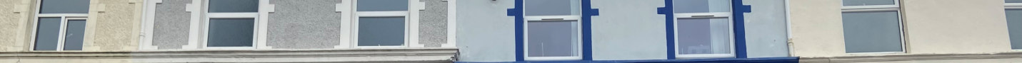 A horizontal photograph showing a section of a building facade with white-framed windows set in textured walls of varying colors including cream, grey, and blue.
