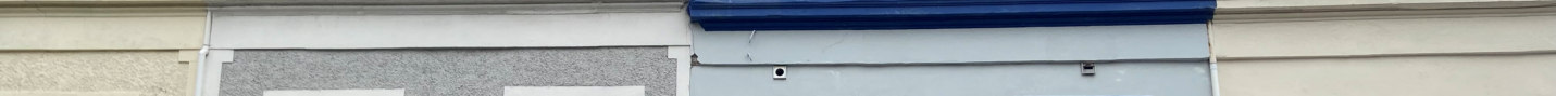 Close-up photograph of a commercial building facade featuring a blue timber fascia board and a grey shuttered shopfront area.