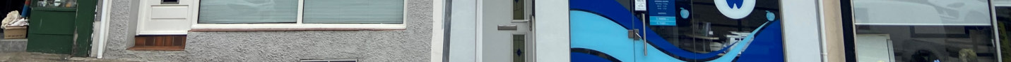 A panoramic street-level photograph showing the exterior of a commercial property with a white door and a shopfront featuring blue branding.
