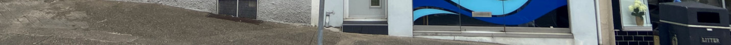 A street-level photograph showing the exterior of a commercial property featuring a distinctive blue wavy shopfront design and a white door next to a gravel slope.
