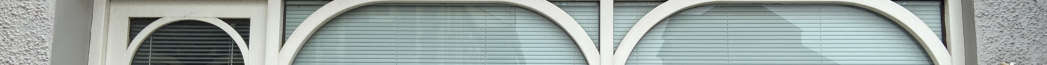 A close-up photograph of a commercial building facade featuring three large arched window openings with white frames and internal blinds.