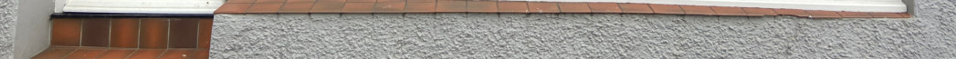 A close-up photograph of a grey textured wall with a tiled ledge and white trim, likely part of a commercial shopfront entrance.