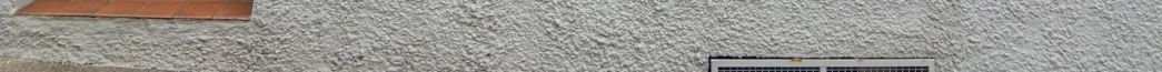 A close-up photograph of a white pebbledash exterior wall showing a section of terracotta roof tiles and a vented grille.