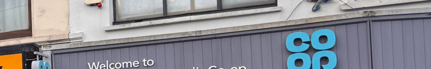 A close-up photograph of a commercial building facade showing a grey timber fascia board with a blue Co-op logo and a window above.