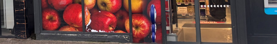 A close-up photograph of a shop front featuring a large window display with a red apple graphic and a black door frame to the left.