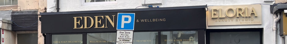 A street-level photograph of a commercial shopfront featuring a black fascia board with gold lettering reading 'EDEN & WELLBEING' and a blue parking sign.