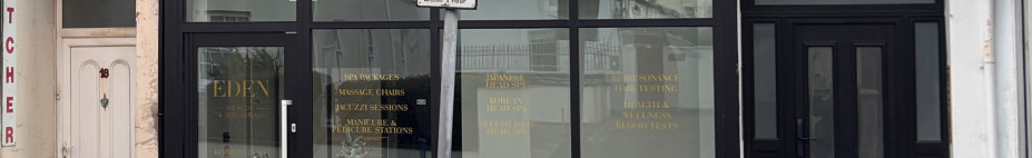 A photograph showing the ground floor frontage of a commercial property with black framed shop windows and a white door to the left.