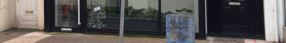 A street-level photograph showing the ground floor facade of a commercial property featuring a black-framed shop window and adjacent doors.