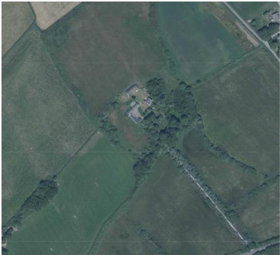 An aerial satellite view showing a rural property with a small cluster of buildings surrounded by green fields and hedgerows.