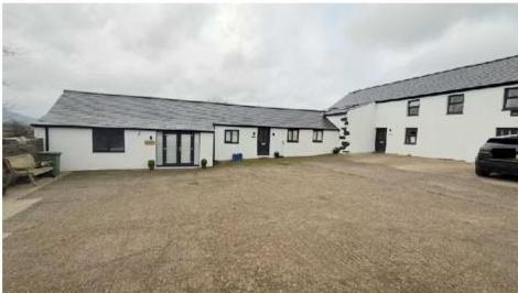 A photograph showing a white, single-story agricultural building with a slate roof and a large gravel yard.