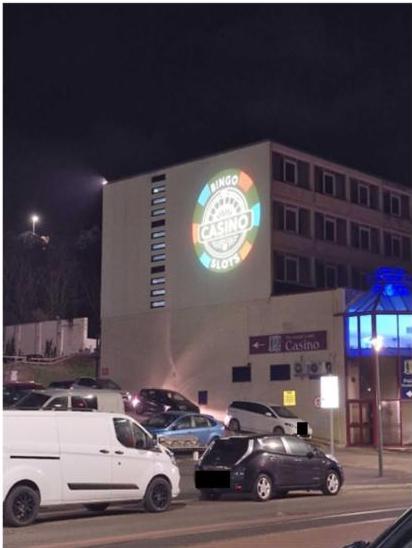 Night-time photograph of a multi-story commercial building with a large illuminated 'Bingo Casino' projection on its facade. Several vehicles are parked in the foreground.