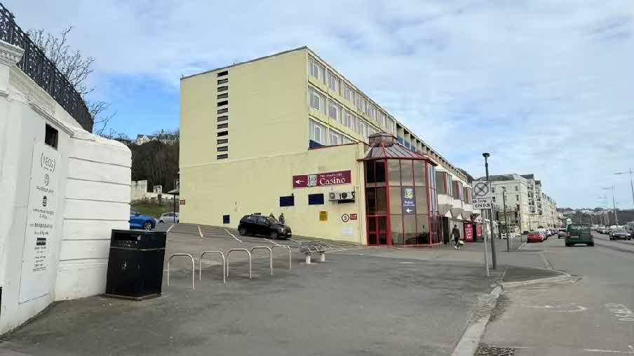 A street-level photograph showing the exterior of the Best Western Palace Hotel and Casino, with a car park area in the foreground containing bike racks and a black bin.